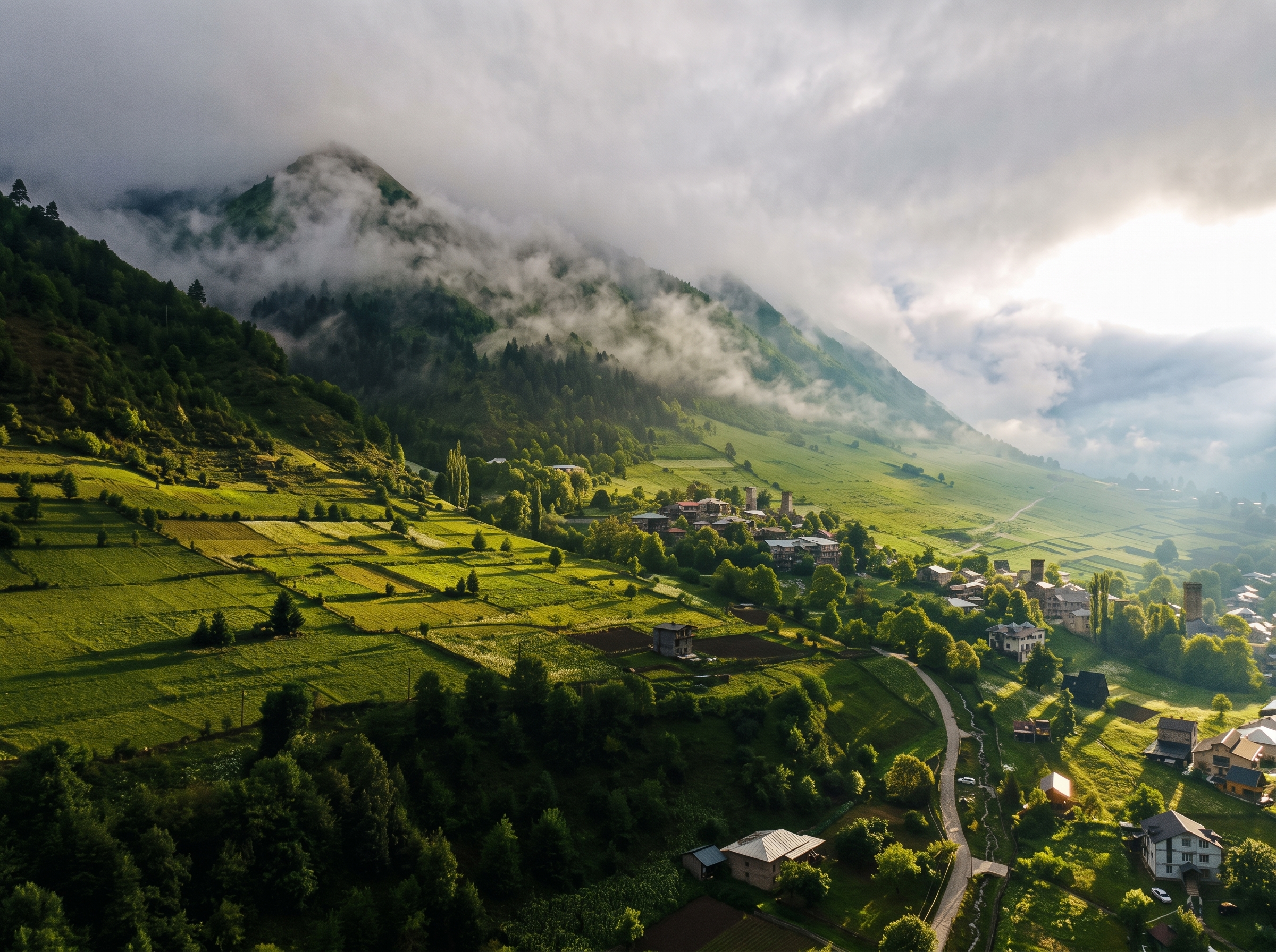 Aerial view of a green mountain valley with a Svaneti village and cloud-covered peaks