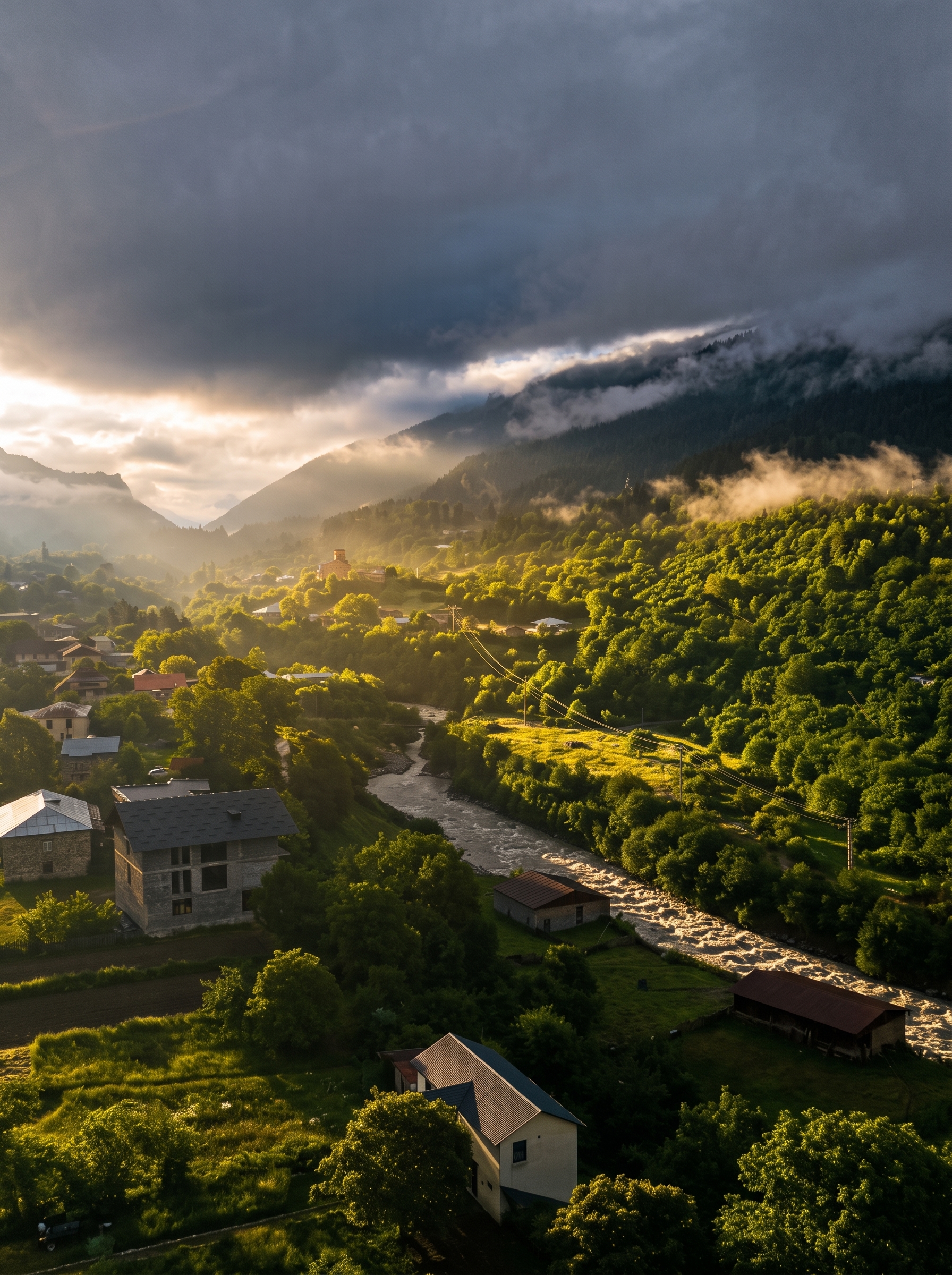 Mountain village and river valley at sunrise with low clouds over forested slopes